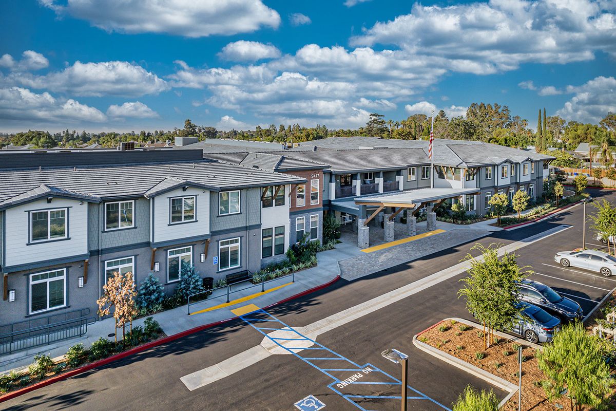 A modern residential building with a spacious parking lot and landscaped surroundings under a partly cloudy sky.