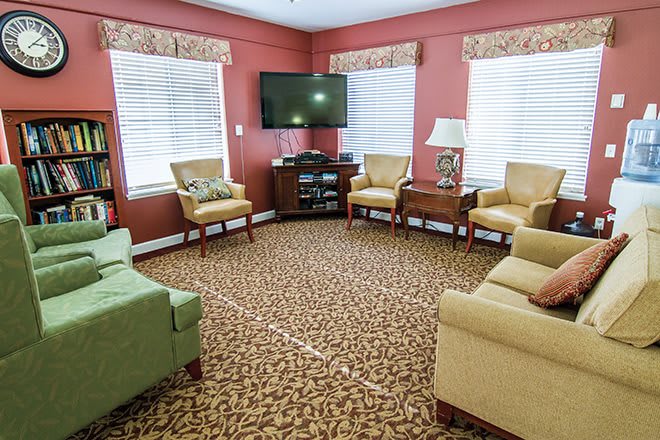 A cozy living room with multiple sofas and chairs arranged around a television on the wall, featuring a patterned carpet and red-painted walls.