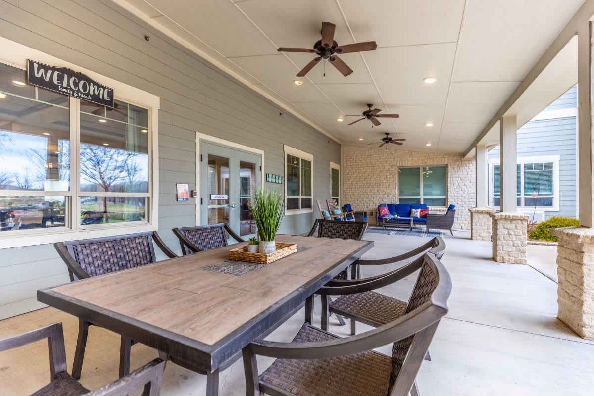A spacious outdoor patio with a large wooden table, surrounded by chairs and decorated with ceiling fans.