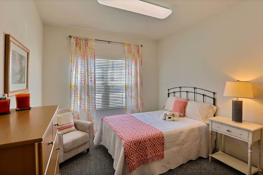 A cozy bedroom with a bed, crib, and chair near a window with colorful curtains.
