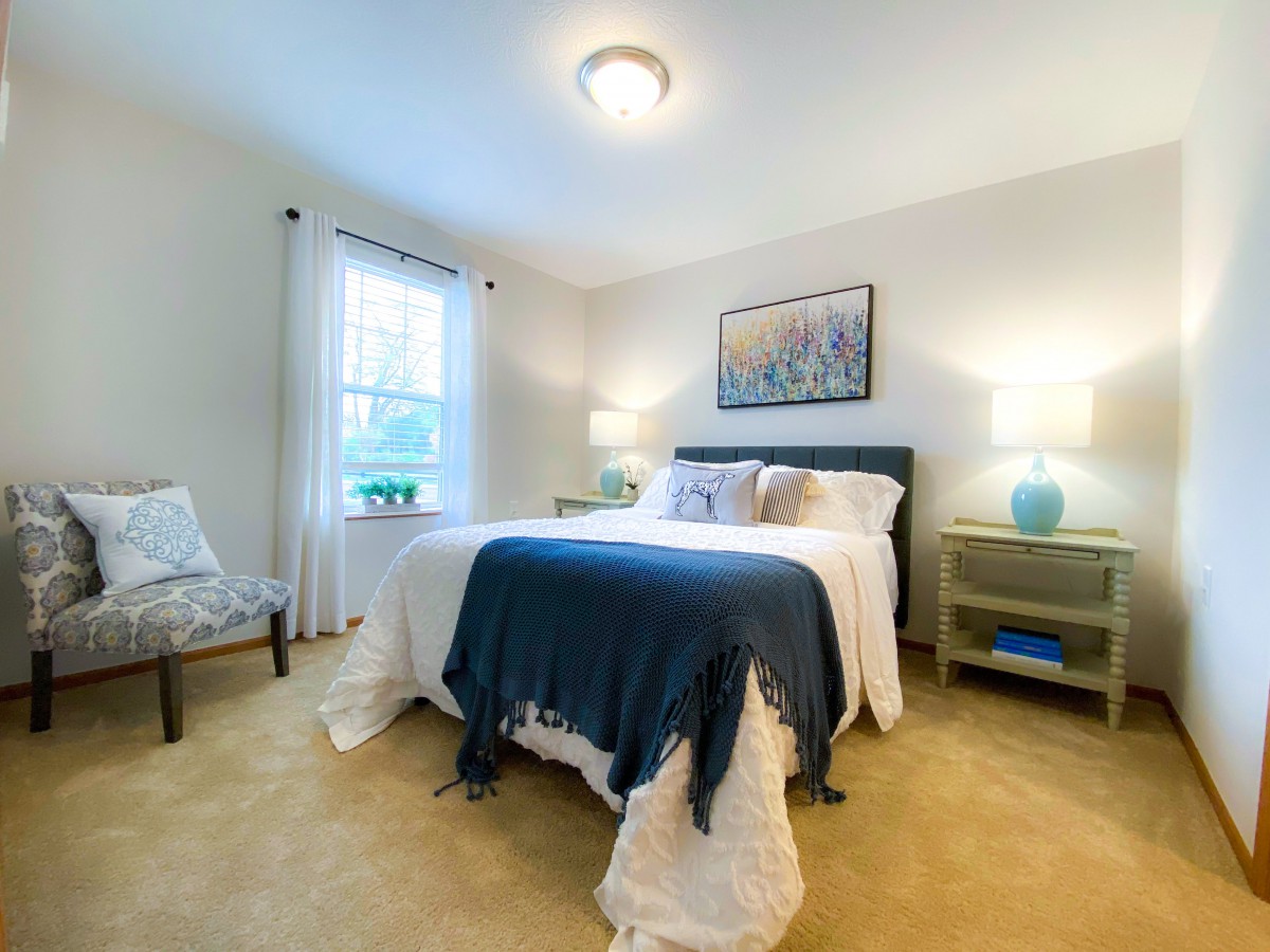 A cozy bedroom with a neatly made bed, two bedside tables with lamps, and a window letting in natural light.