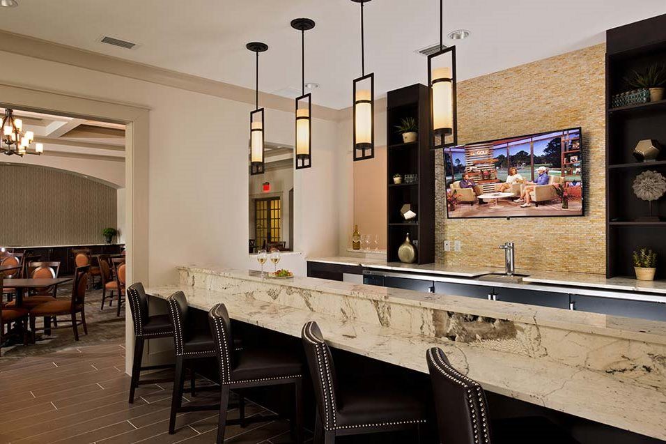 A modern bar interior featuring a marble counter, stylish pendant lights, and a mounted television.