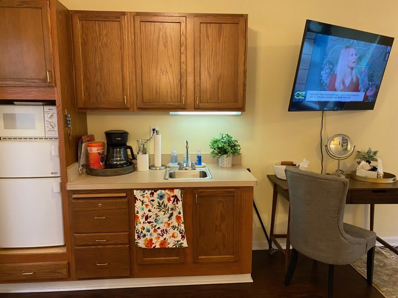 A cozy kitchenette with wooden cabinets, featuring a coffee maker and a wall-mounted TV.