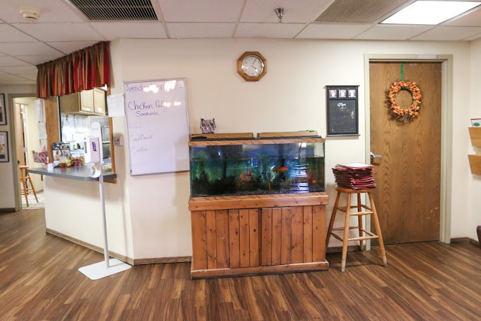 A room interior featuring a fish tank on a wooden stand, a whiteboard, and a stool.