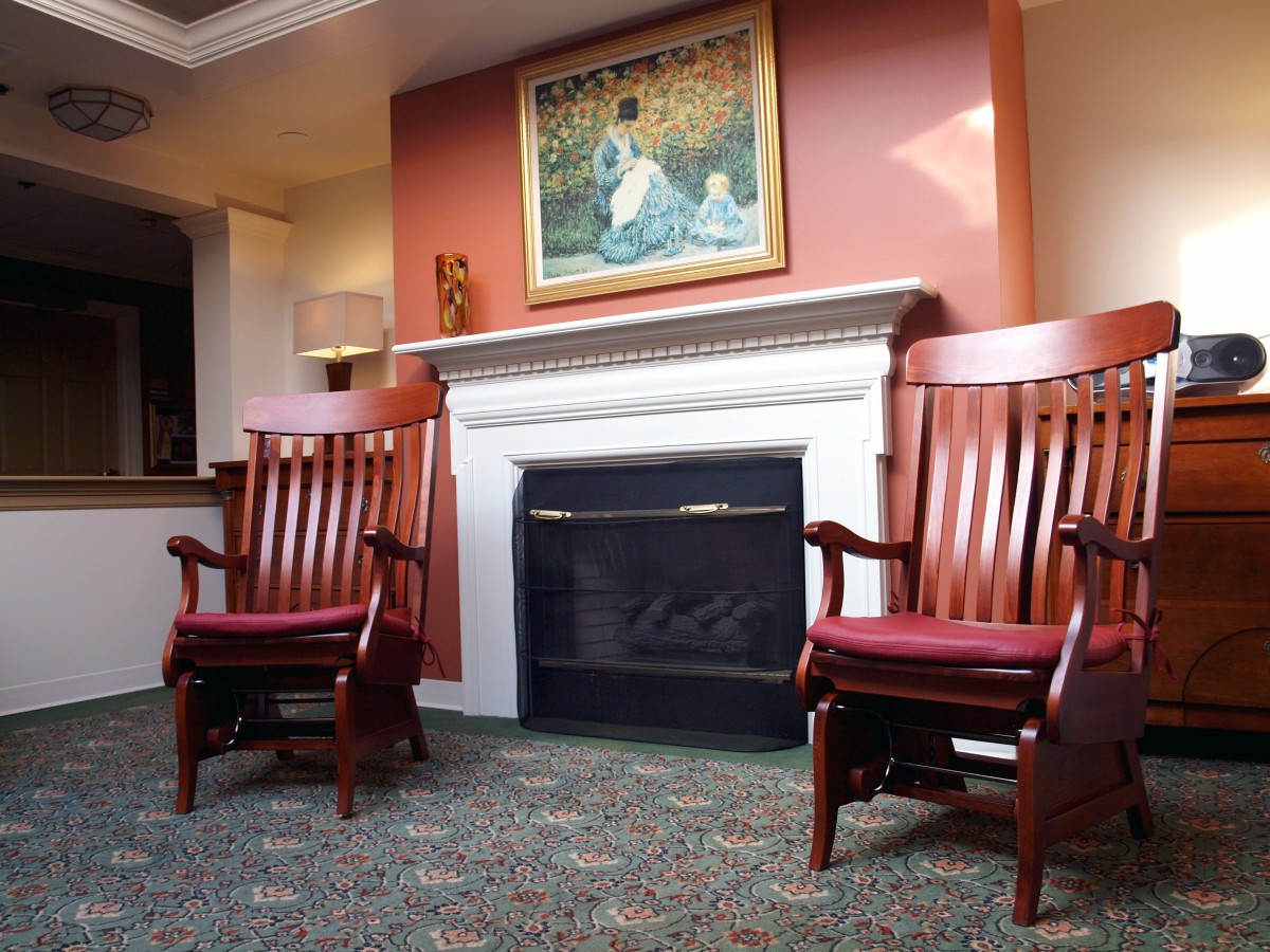 A cozy living room with two wooden rocking chairs flanking a fireplace, adorned with framed artwork above.