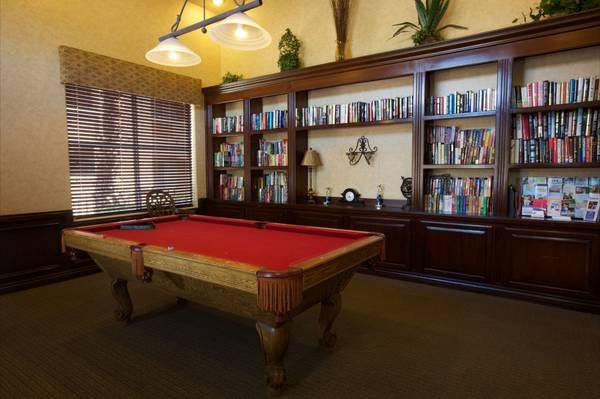 A luxurious library with a red felt pool table and wooden bookshelves filled with books.