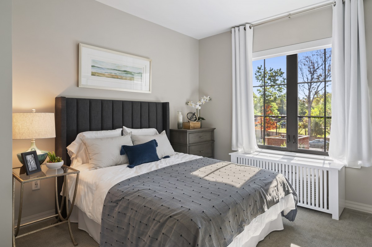A modern and cozy bedroom with natural light streaming through a large window, featuring elegant decor and a neatly made bed.
