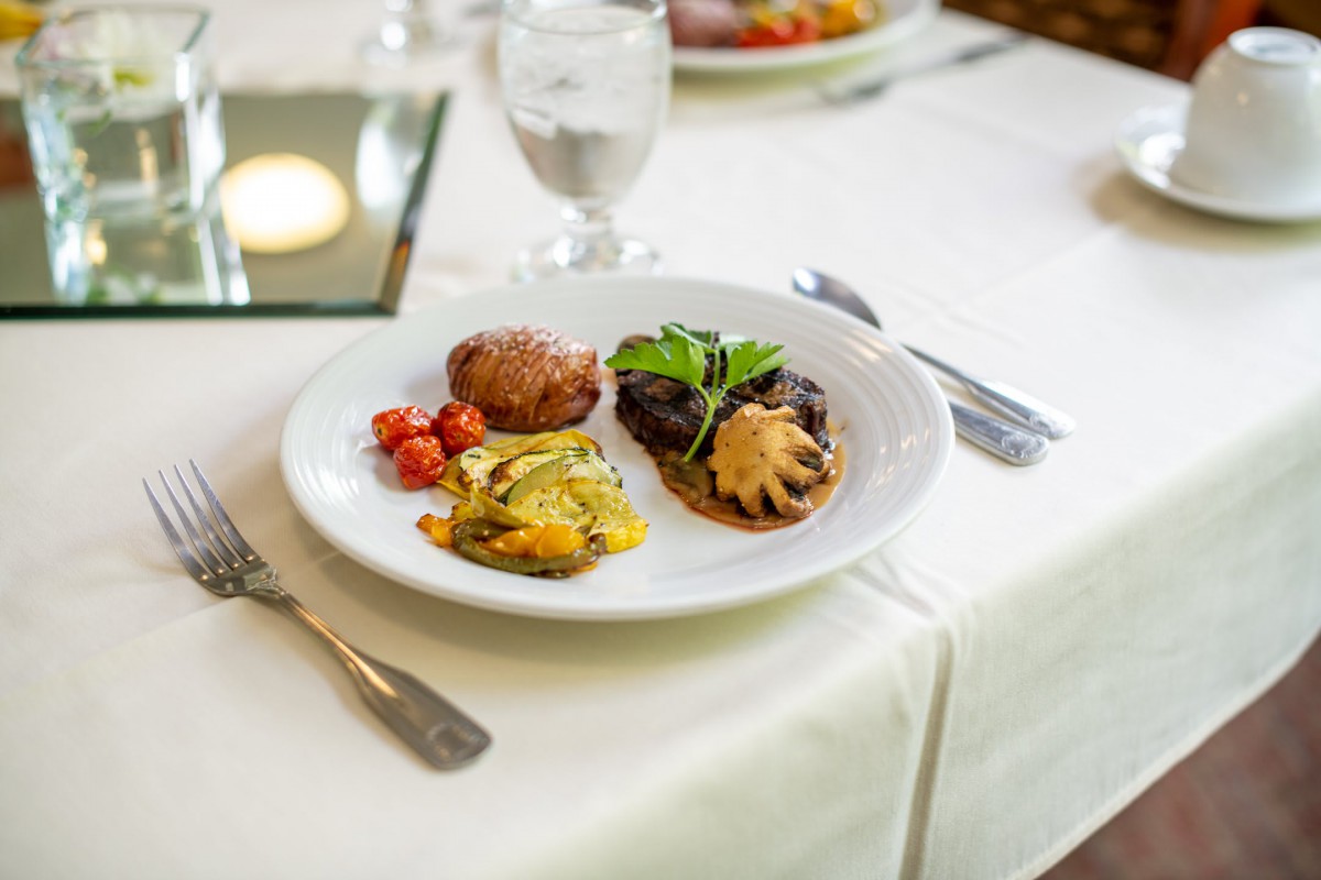 A gourmet meal featuring meat with sauce, vegetables, and a side, elegantly presented on a white tablecloth.