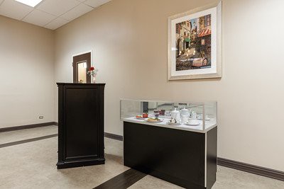 A museum interior featuring a glass display case with various objects and a framed painting on the wall.