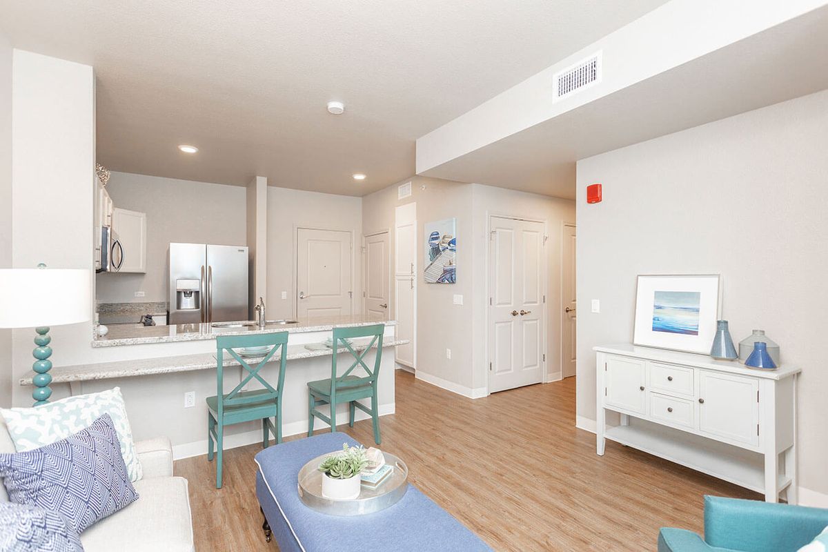 A modern apartment interior featuring a kitchen with bar stools and wood flooring.