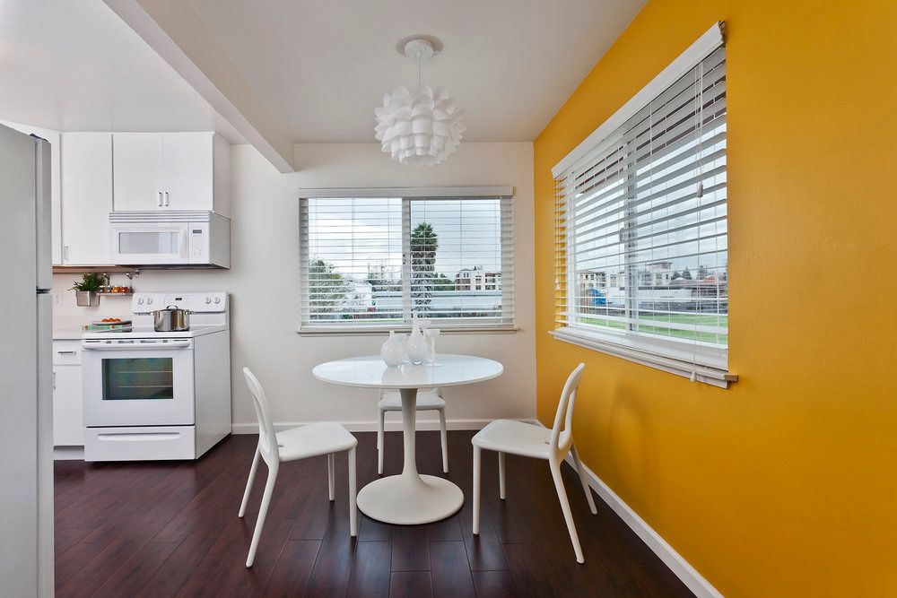 A modern, minimalist dining area with white furniture and a striking yellow accent wall.