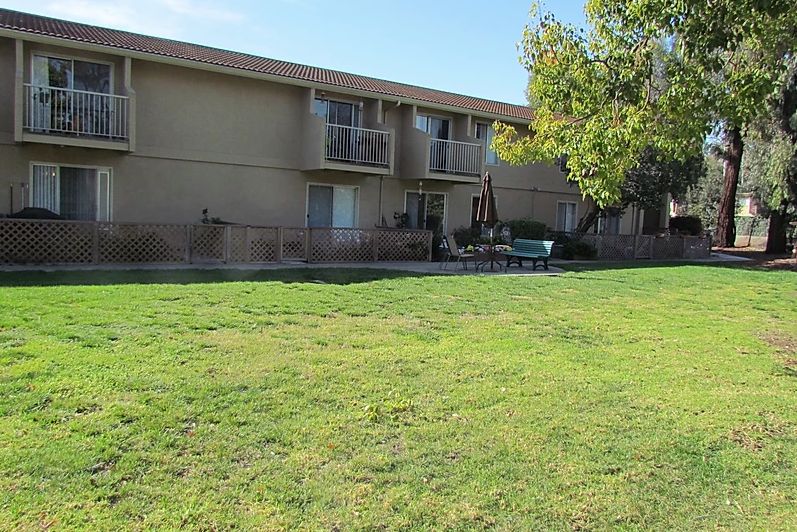 A residential building with balconies overlooking a grassy area and trees.