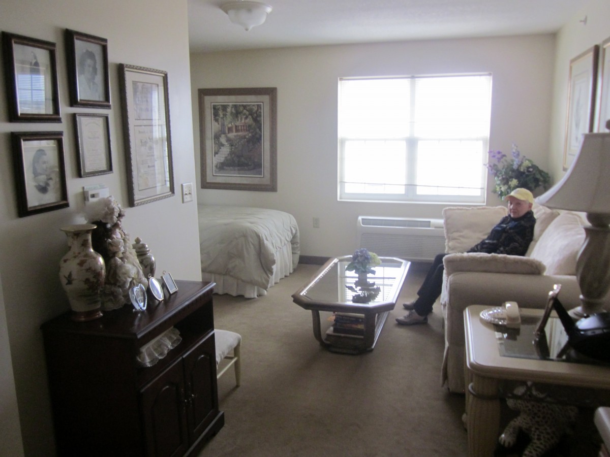 A cozy apartment space with a combined living and bedroom area, featuring comfortable seating and artwork on the walls.