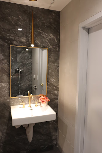 A stylish and modern bathroom featuring a marble wall, elegant mirror, and gold accents.