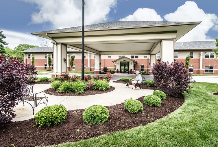 A well-maintained building entrance with landscaped gardens and a paved walkway under a covered entry.