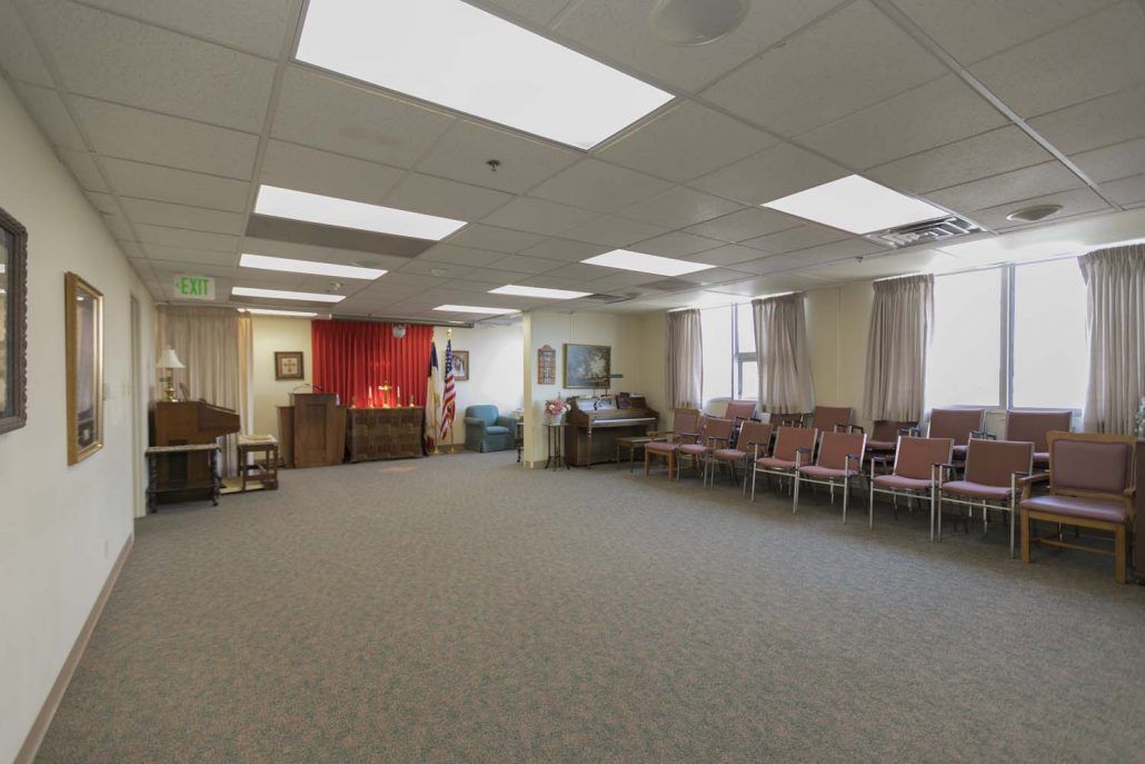 An empty meeting room with a carpeted floor and rows of chairs along the walls.