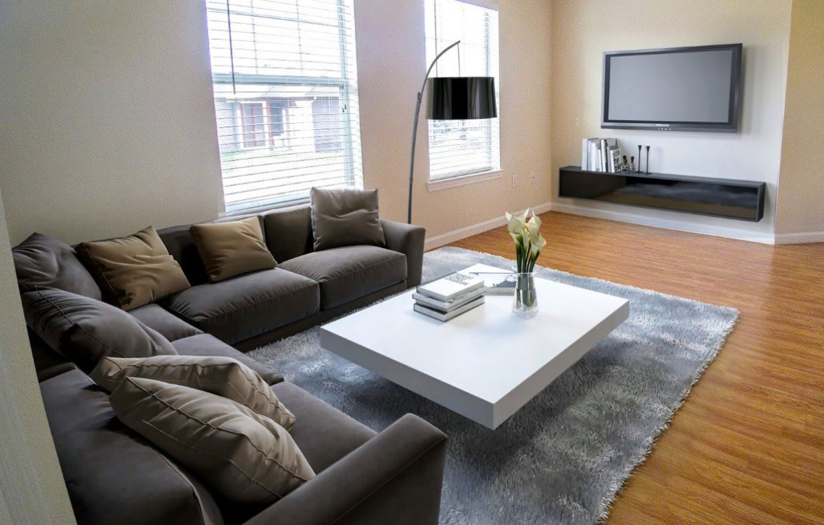 A modern living room featuring a gray sofa, white coffee table, and wall-mounted TV, with large windows providing natural light.