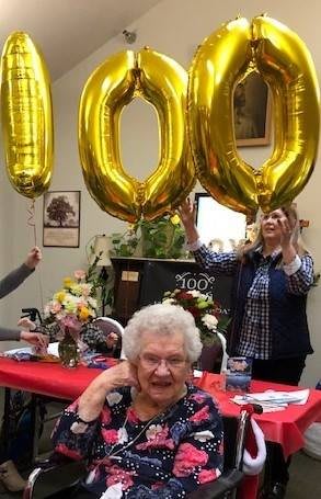 A joyful celebration of a 100th birthday with balloons and smiles.
