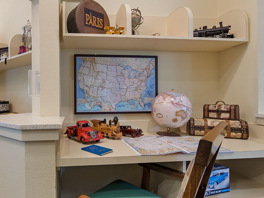 A study desk with a map of the USA on the wall, a globe, toy vehicles, and shelves holding books and decorations.