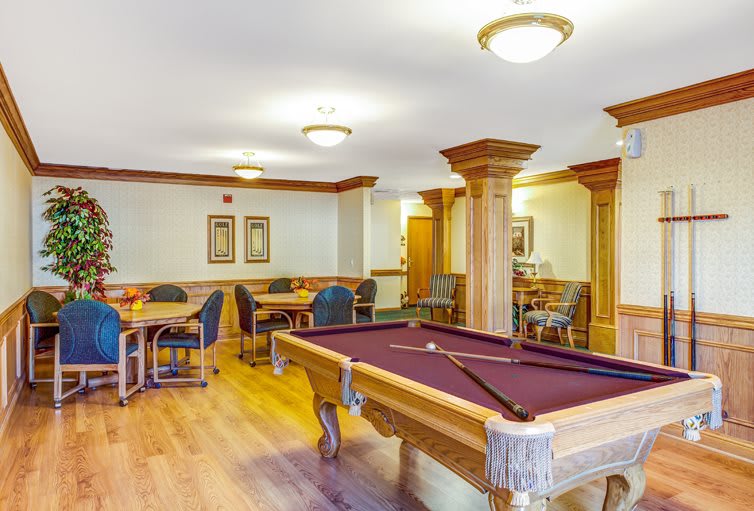 A recreation room featuring a pool table, tables, and chairs with wooden flooring.