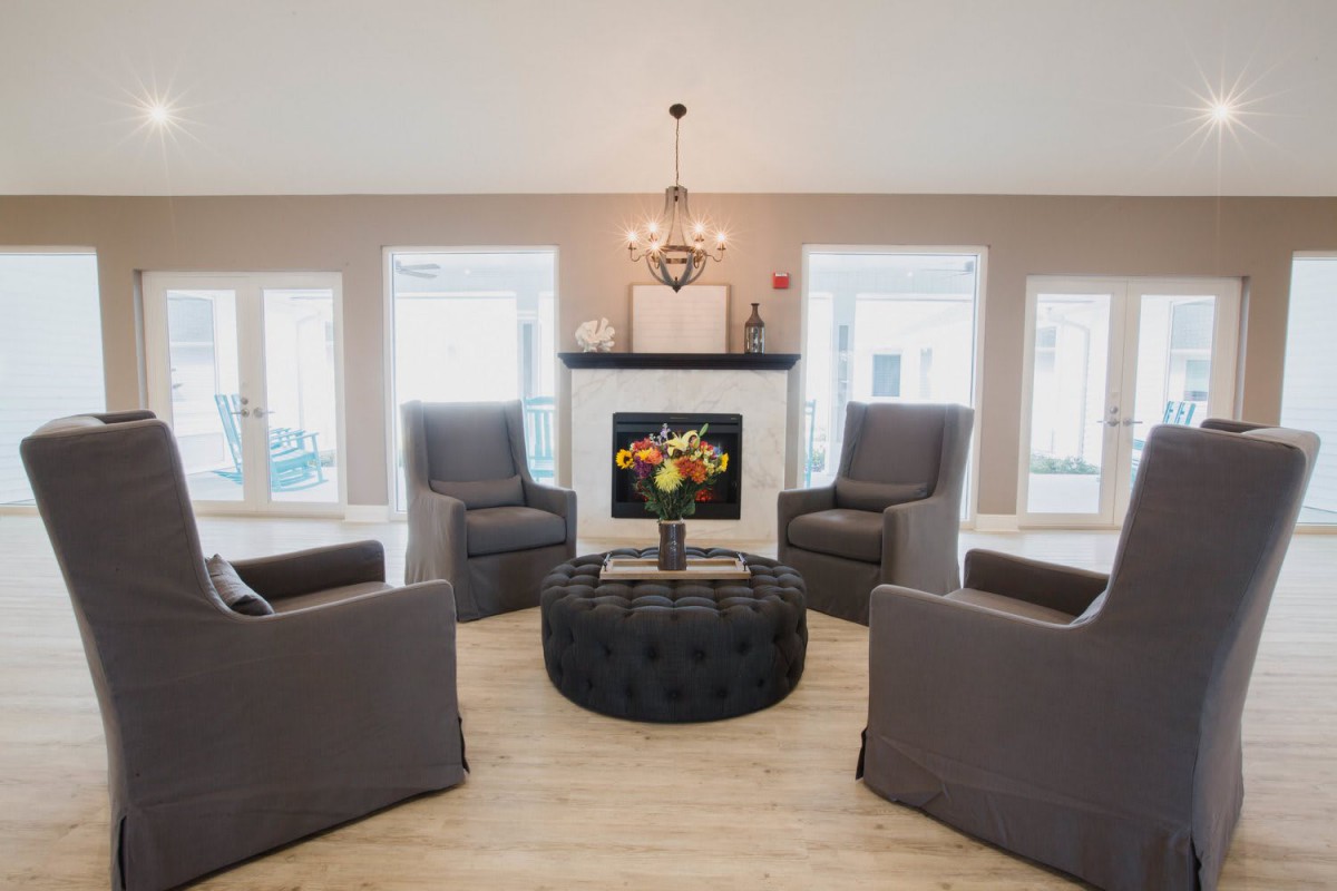 A modern living room with four gray chairs arranged around a central fireplace and a round ottoman.
