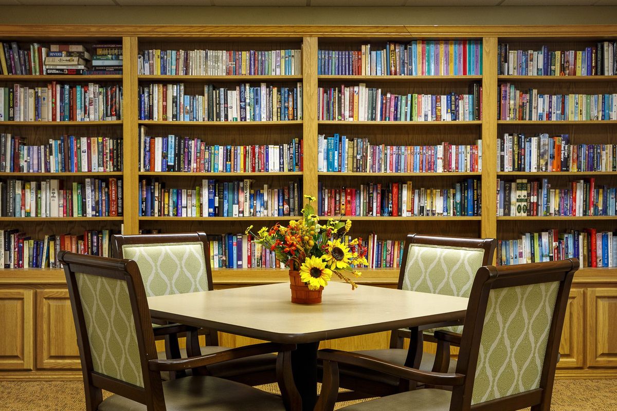 A cozy library reading area with a table, chairs, and bookshelves filled with books.