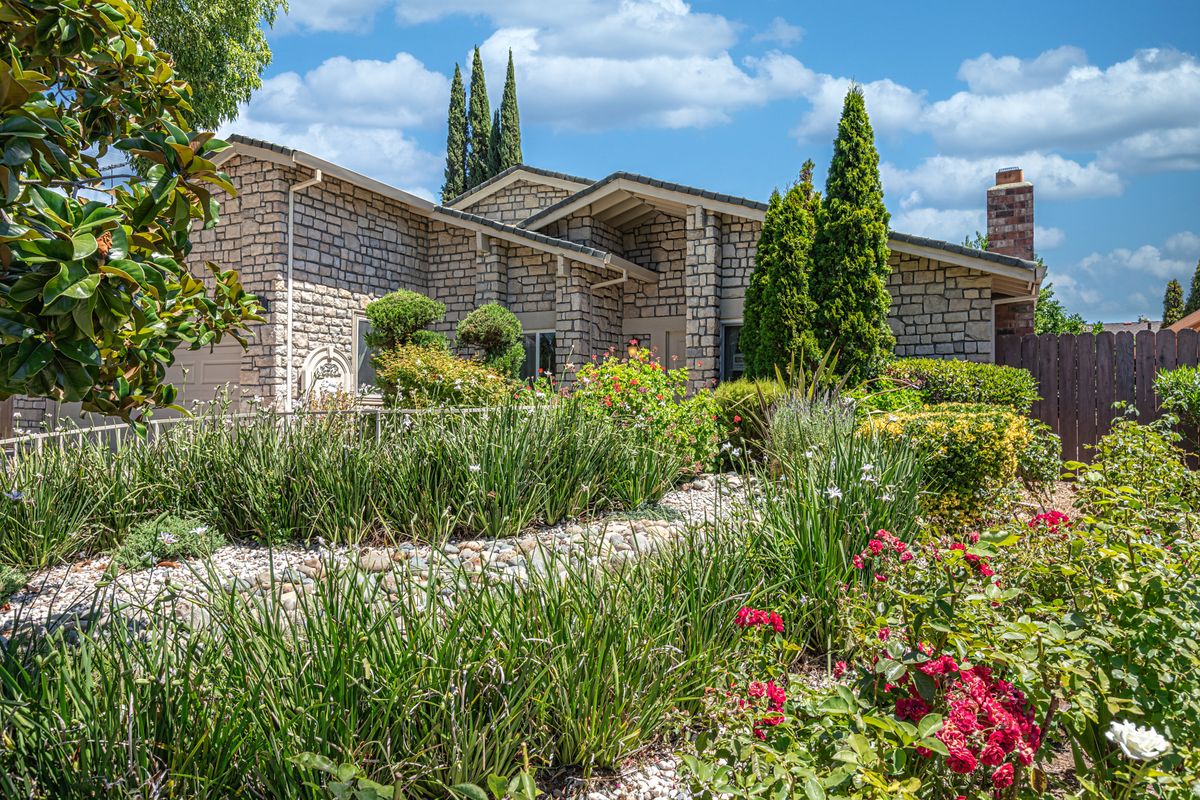 A beautiful house surrounded by lush gardens and vibrant flowers under a clear blue sky.