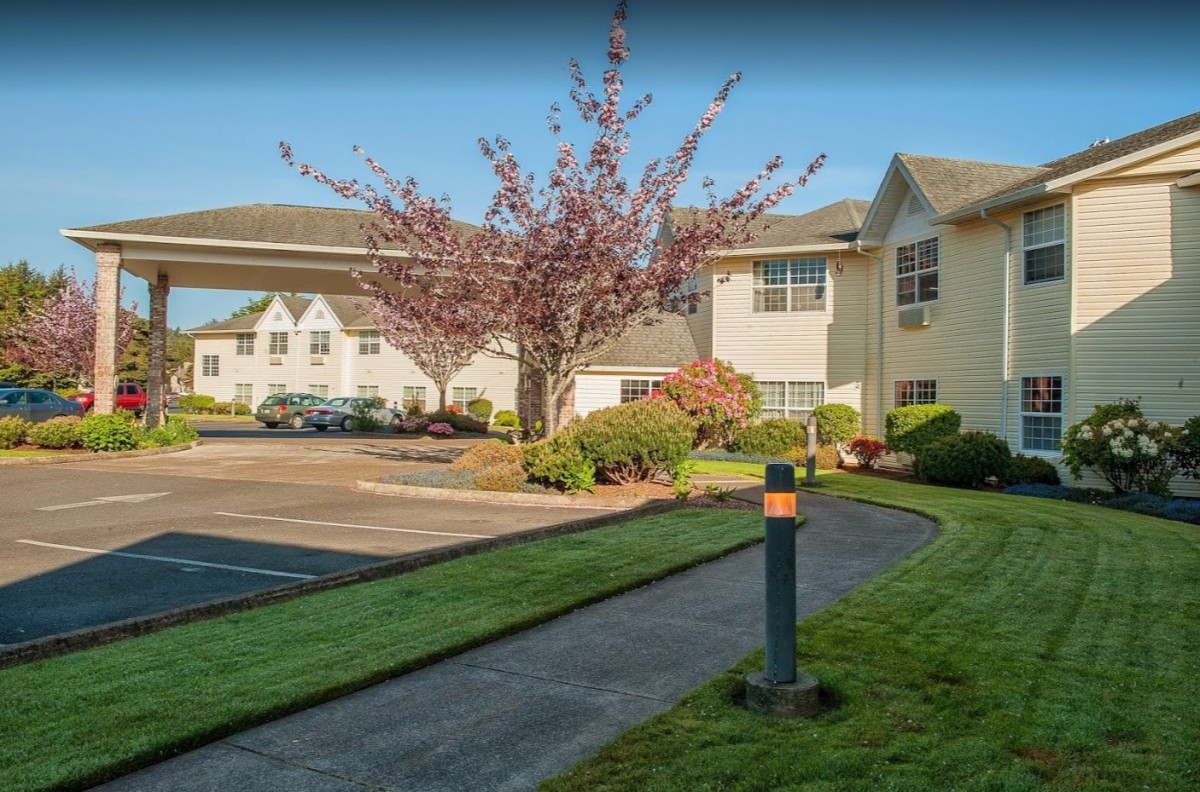 A view of a building with a landscaped garden and parking lot in the foreground.