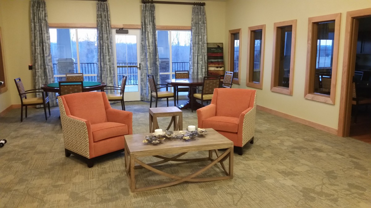 A cozy living room setup with two orange chairs, a wooden coffee table, and large windows with curtains.
