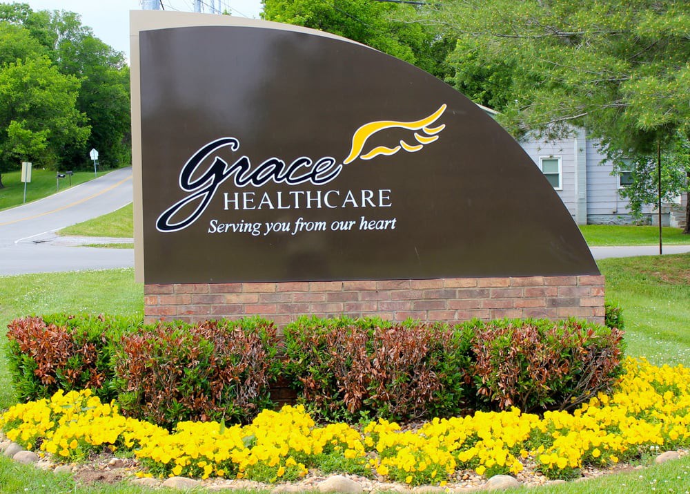 An outdoor sign for Grace Healthcare with a landscaped area featuring yellow flowers.