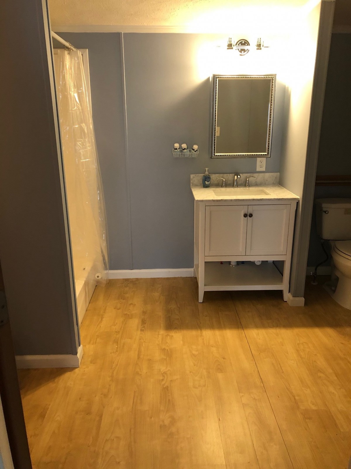 A modern bathroom with a wooden floor, featuring a vanity, sink, and mirror.