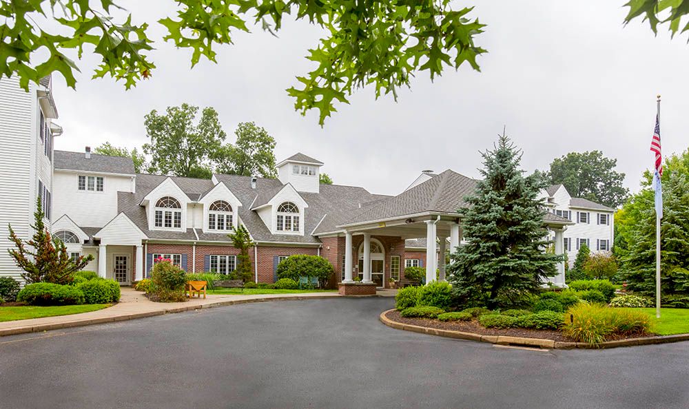 A large residential building with a landscaped driveway and trees surrounding the entrance.