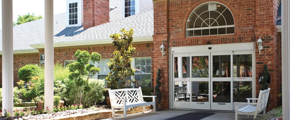 A building entrance with a white bench and greenery.