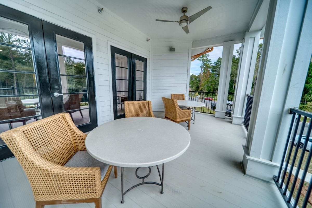 A cozy patio area with a round table and wicker chairs, featuring a ceiling fan and surrounded by glass doors.