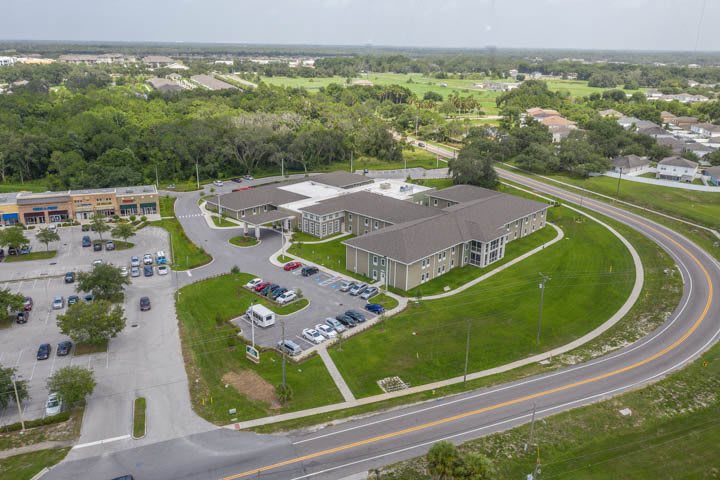 Aerial view of a building with a surrounding parking lot and lush greenery.