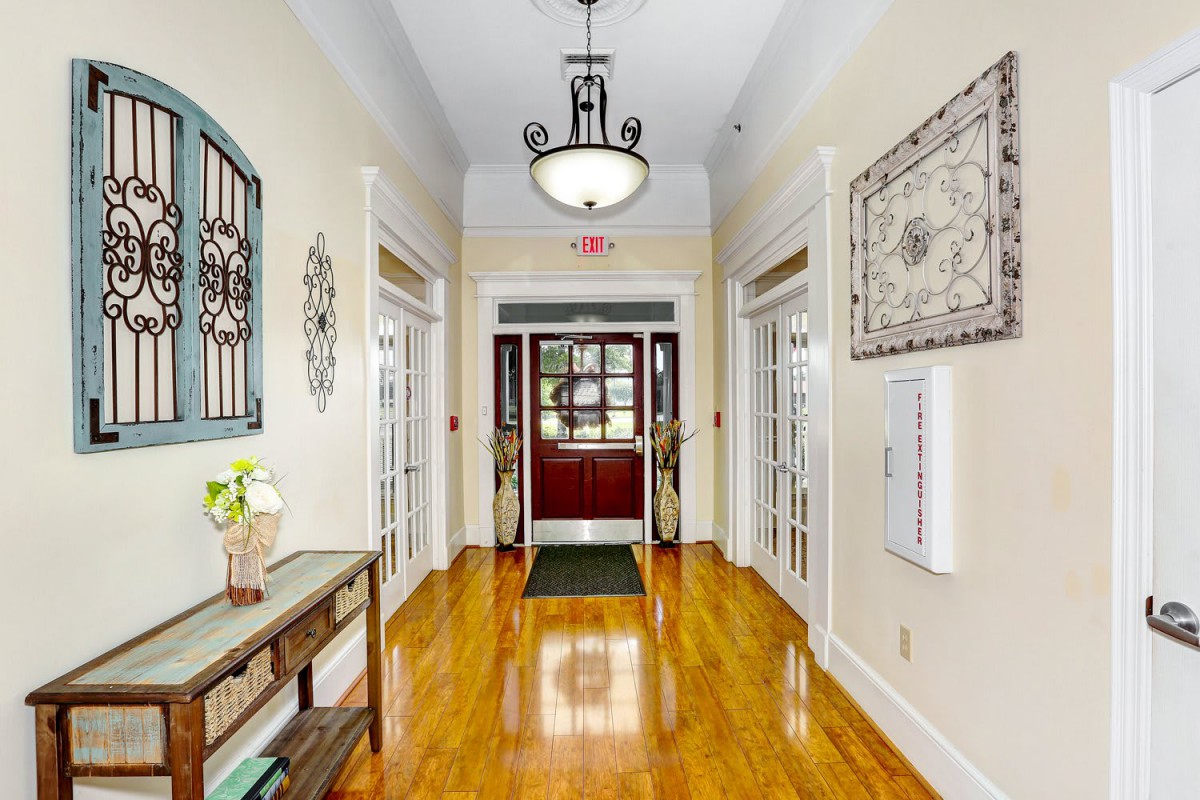 A beautifully decorated hallway with polished wood floors, a chandelier, and double doors at the end.