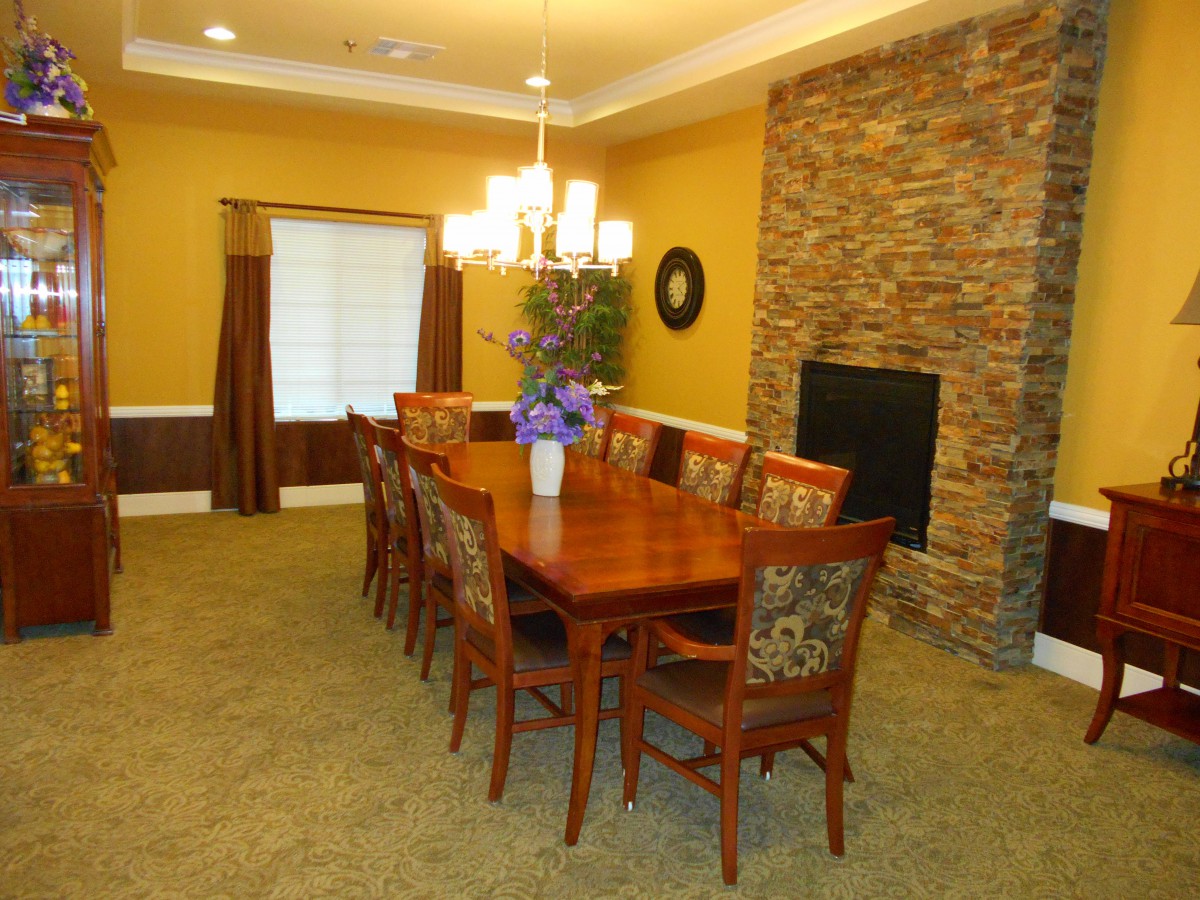 A well-appointed dining room featuring a long wooden table surrounded by chairs, a chandelier overhead, and a stone accent wall.