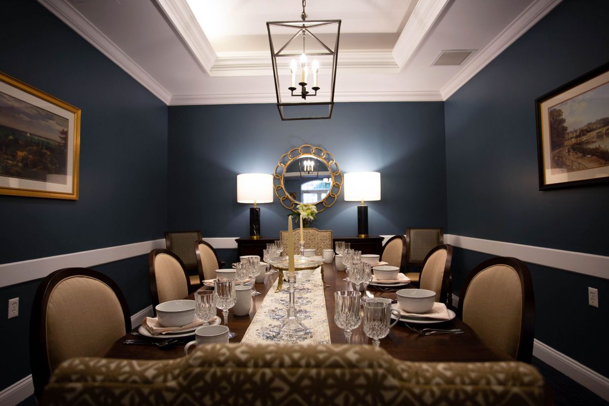 An elegantly set dining room with a mirror and chandelier, featuring dark blue walls and formal tableware.