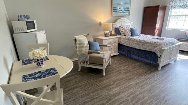 A cozy bedroom with coastal decor featuring a bed, armchair, small table, and warm lighting.