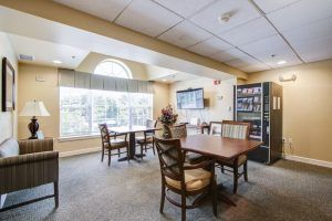 A cozy dining area with tables and chairs, featuring large windows and a vending machine.