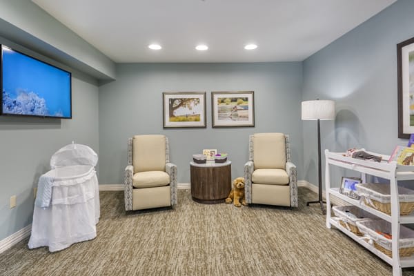 A cozy living room featuring two comfortable chairs, a small round table, artwork on the walls, and a standing lamp in a carpeted area.