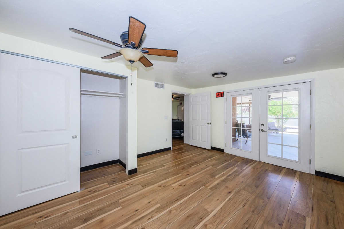 An empty room with hardwood floors, a ceiling fan, and double doors leading outside.