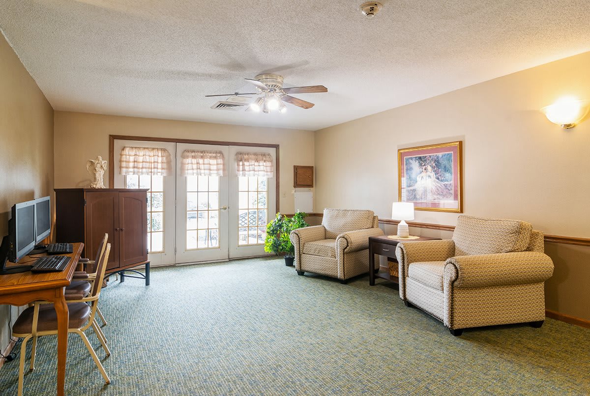 A cozy living room with armchairs, a lamp, and natural light streaming through large windows.