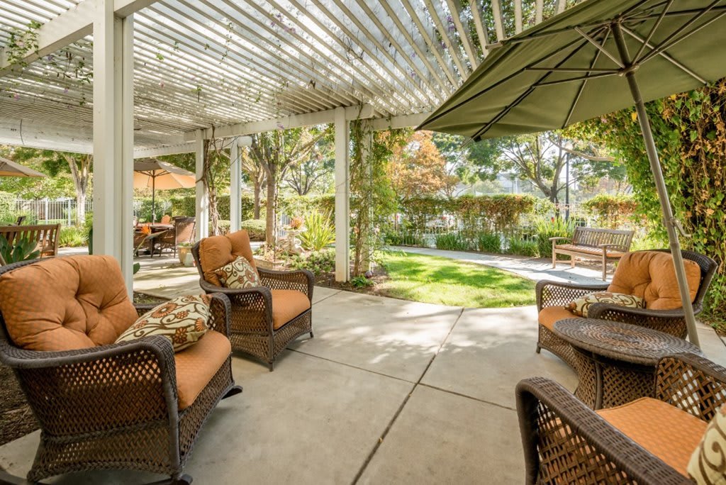 A cozy patio with wicker furniture under a pergola, surrounded by a lush garden.