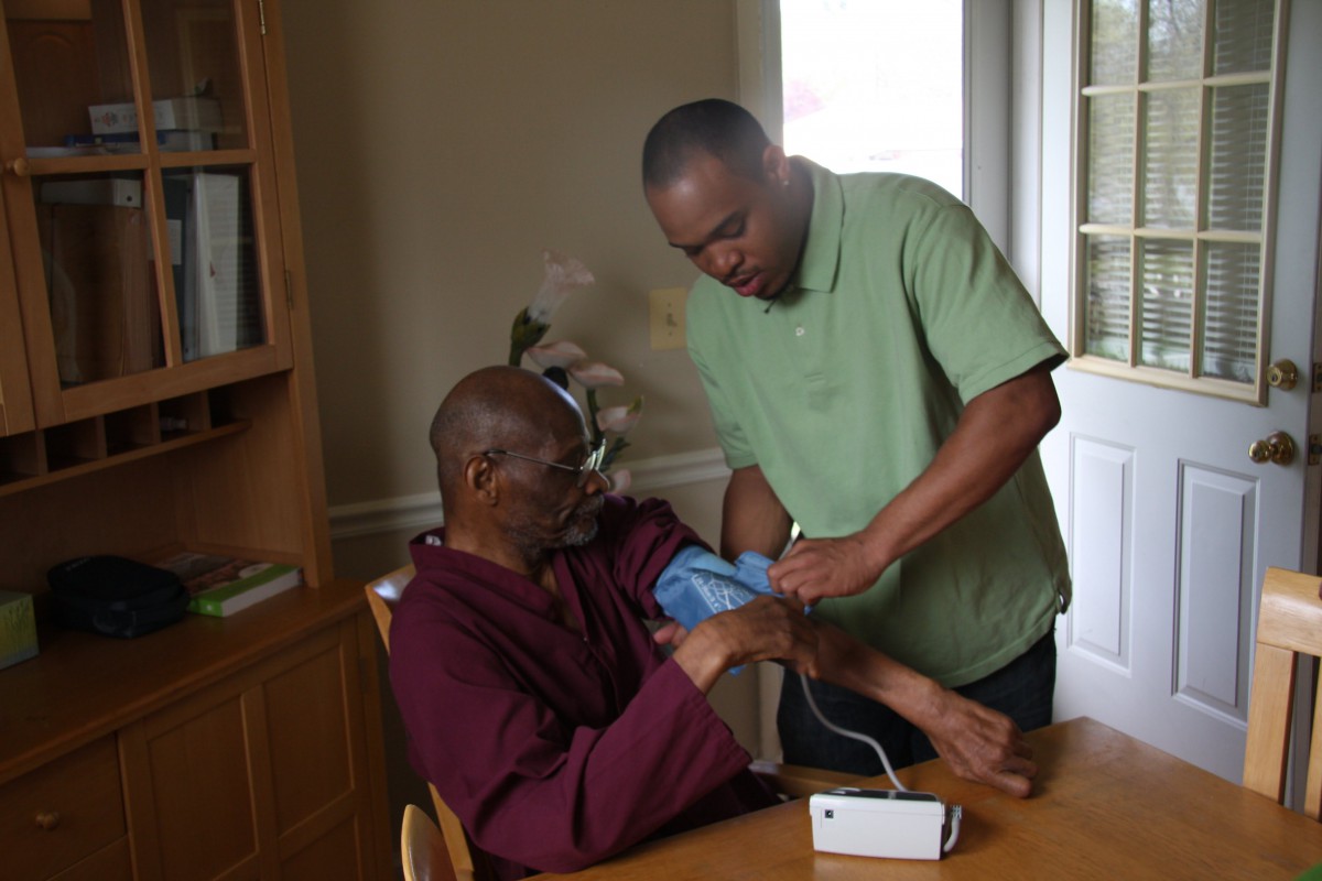 A caregiver assists a senior by monitoring their blood pressure at home.