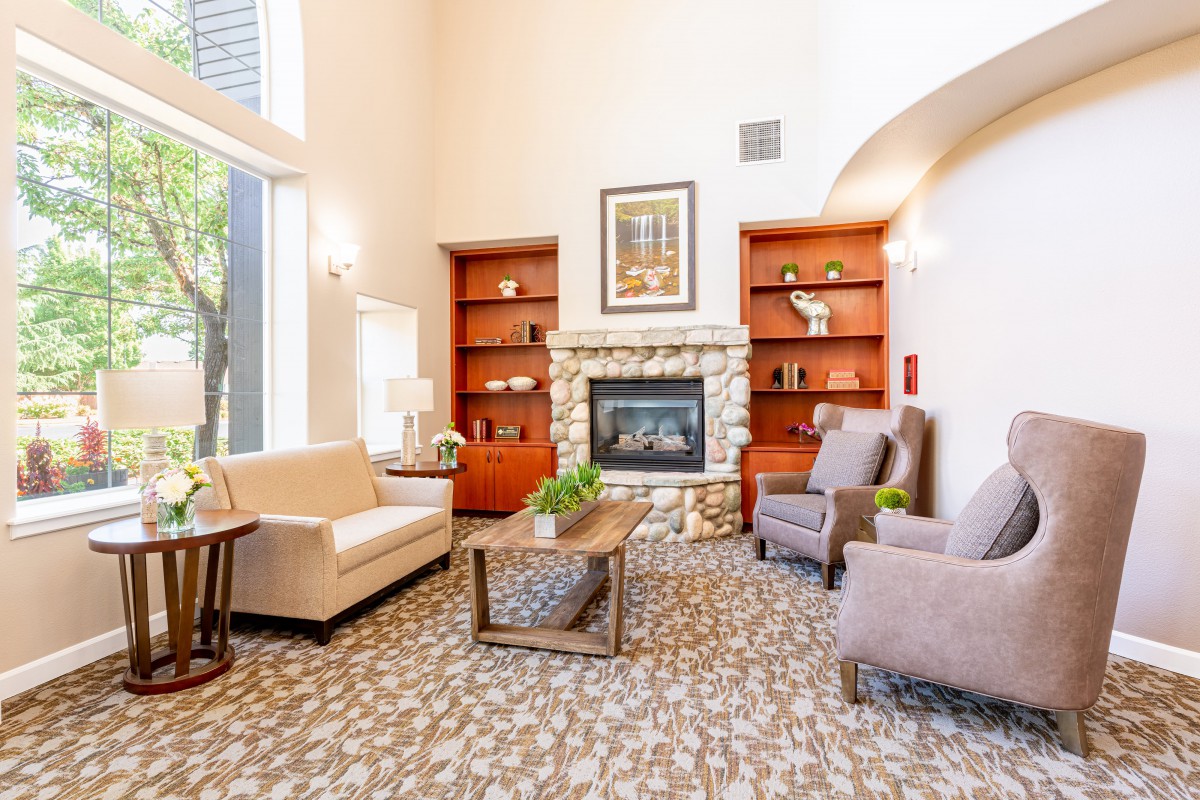 A cozy living room with a fireplace, comfortable seating, and built-in bookshelves, illuminated by natural light.