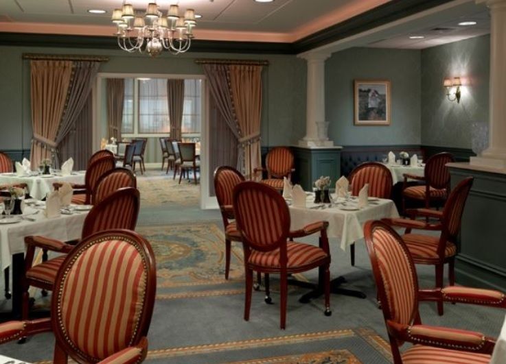 An elegant dining room with neatly arranged tables and chairs, featuring a chandelier and decorative curtains.
