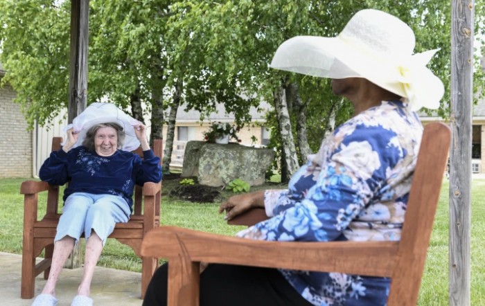 Two people sitting on benches in a park, wearing large hats and engaging in conversation.
