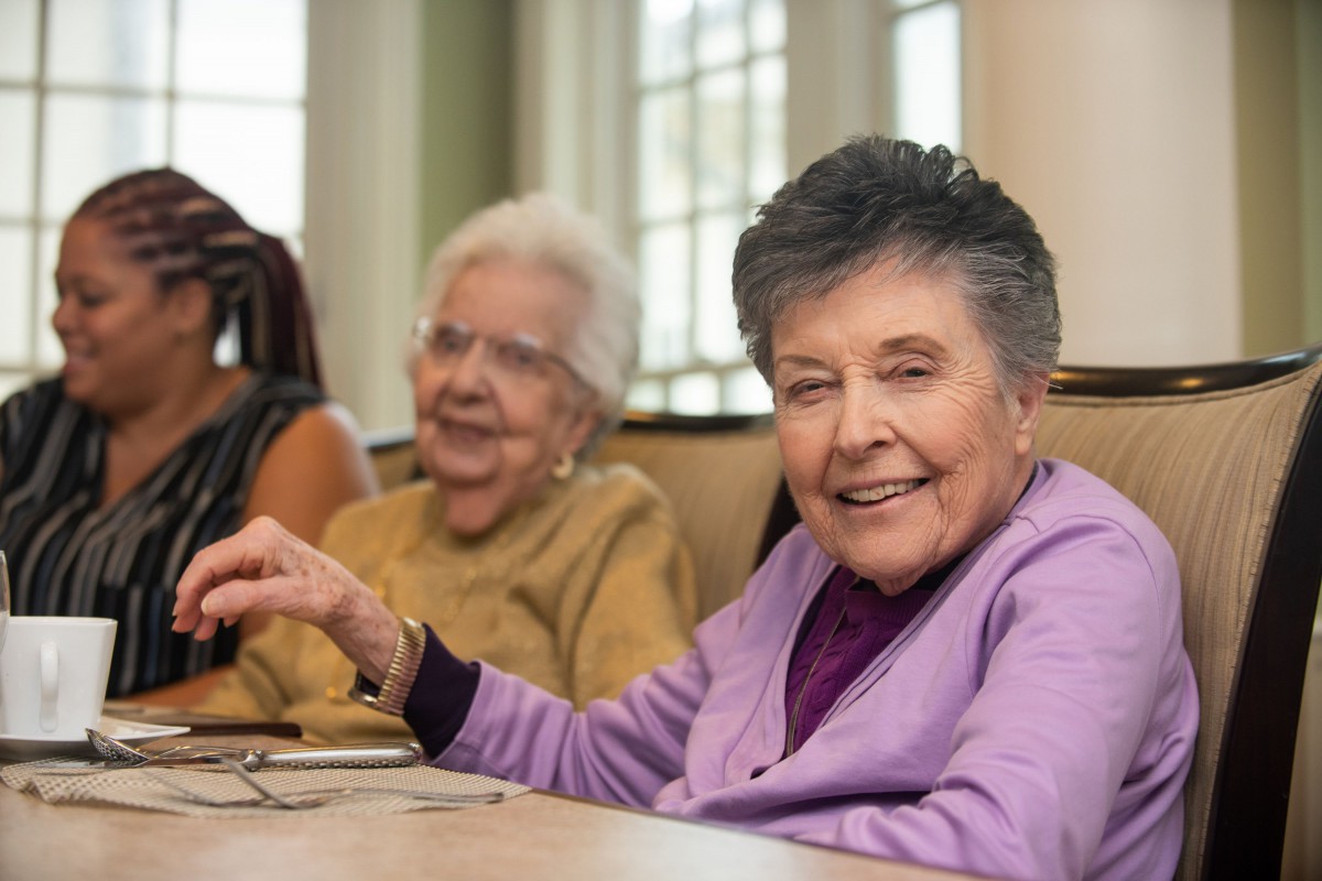 A group of elderly women smiling and sitting together indoors.