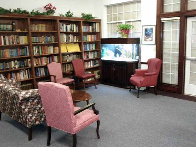 A cozy library corner with bookshelves, armchairs, and an aquarium.